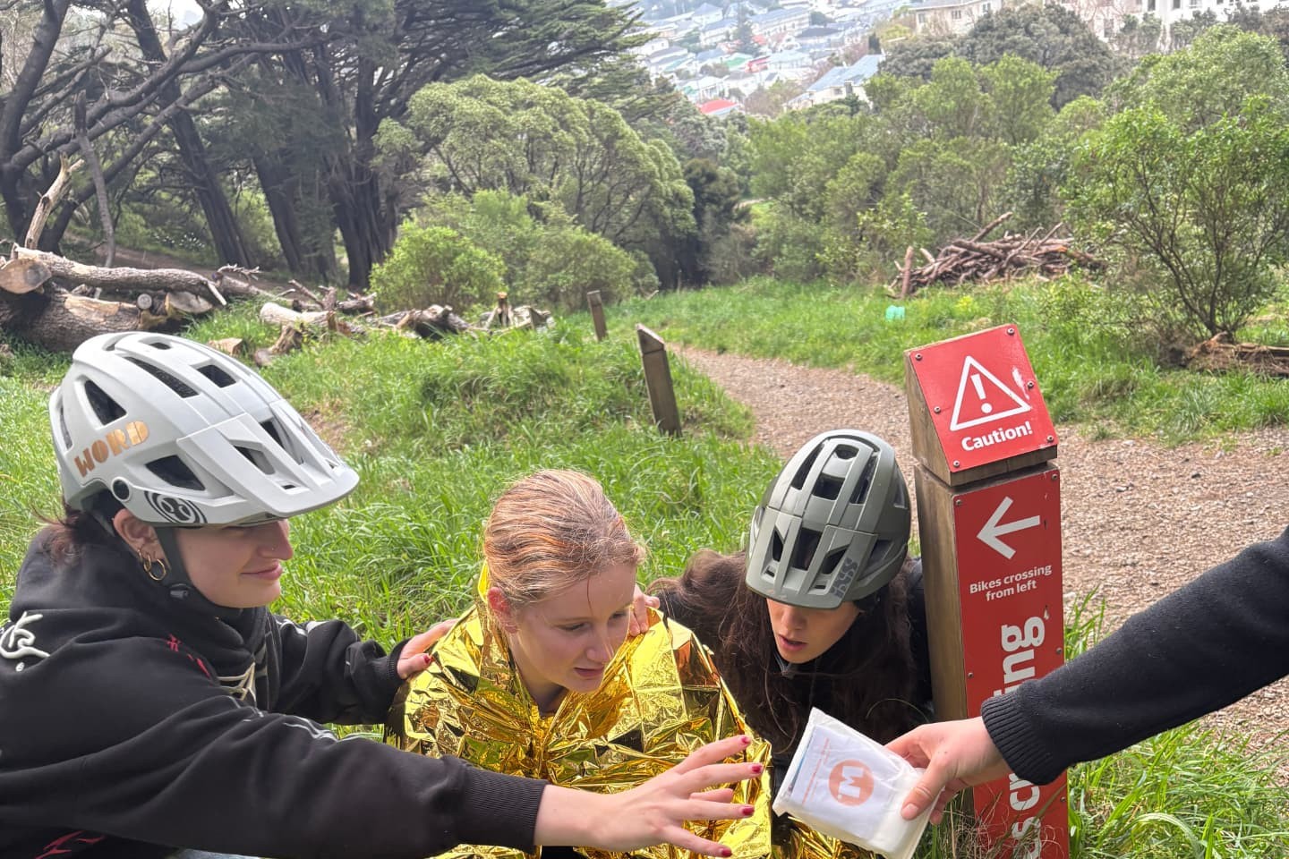 Teenage mountain bikers helping a friend wrapped in an emergency blanket while a WORD first aid kit is passed over